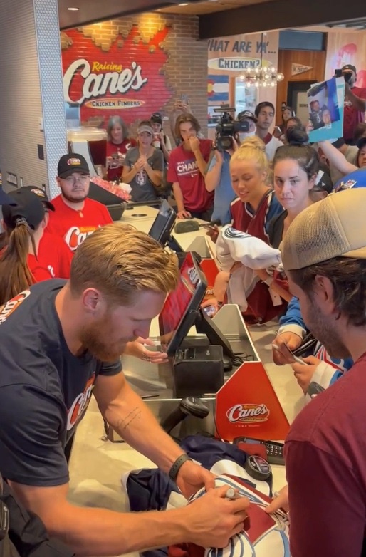 A professional hockey player signing a jersey for fans at a restaurant brand event