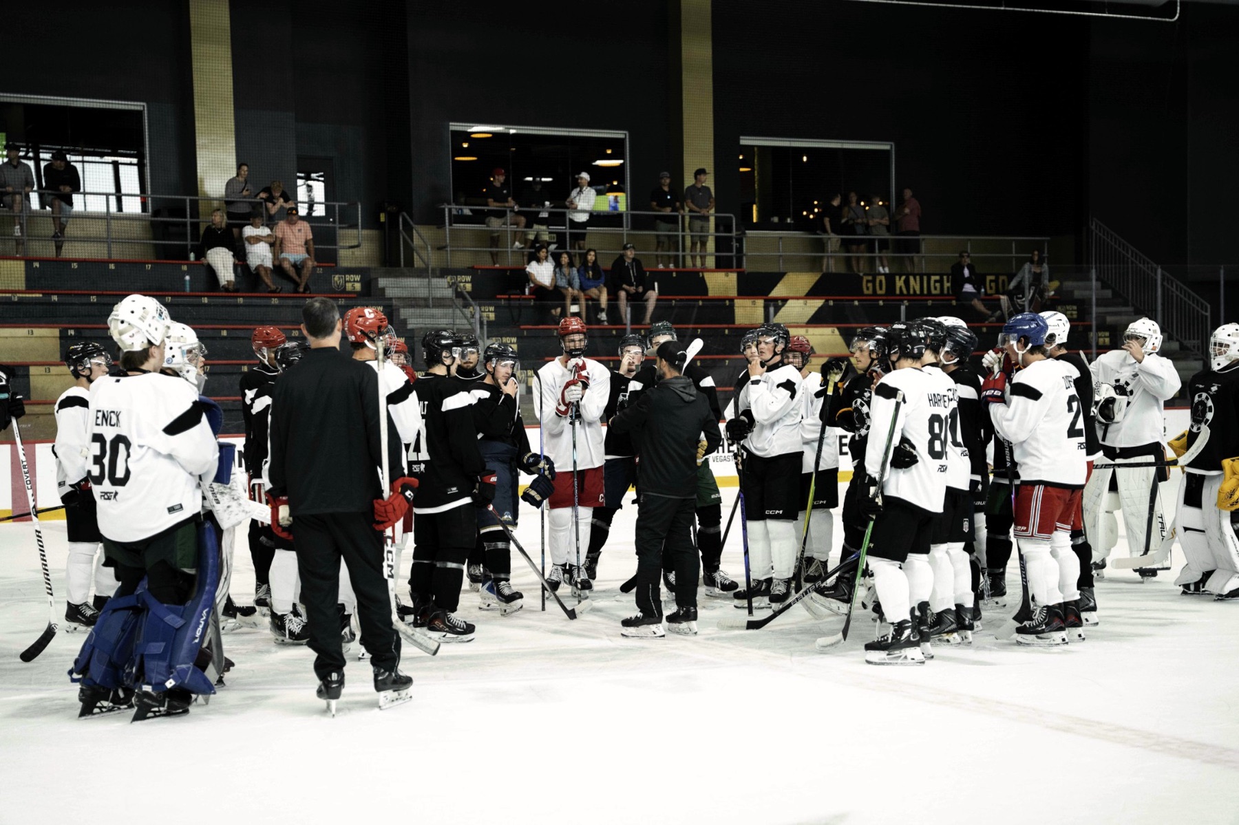 Hockey players in full gear gathered around a coach on the ice at a summer camp